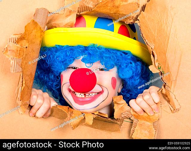 young child dressed as a clown with wig and fake nose has fun watching from the open cardboard