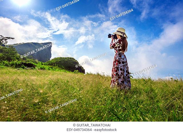 Woman standing on meadow and holding camera take photo at Phu Chi Fa mountains in Chiangrai, Thailand. Travel concept