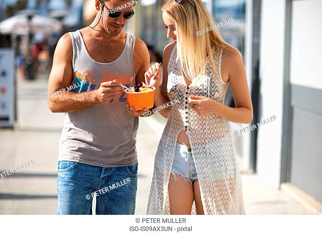 Couple strolling and eating frozen yoghurt on sidewalk, Venice Beach, California, USA