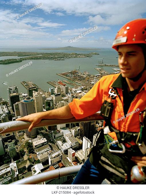 Young man with climbing equipment on top of Sky Tower, view at Central Business District and Waitemata Harbour, Auckland, North Island, New Zealand