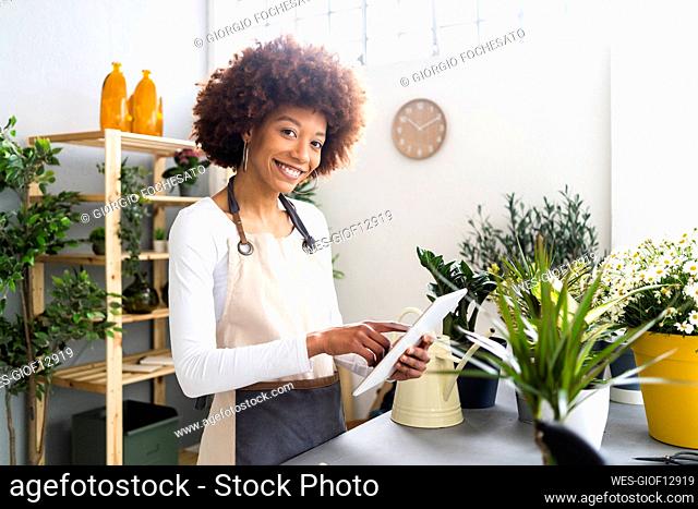 Smiling female florist holding digital tablet by potted plants at store