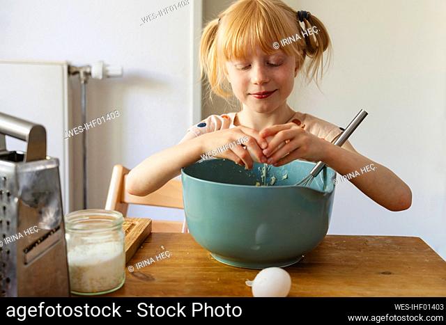 Smiling girl breaking egg into bowl at home