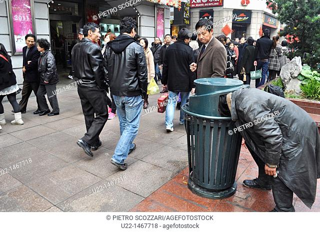 Shanghai (China): a homeless man looking for something to eat into a garbage can in East Nanjing Road