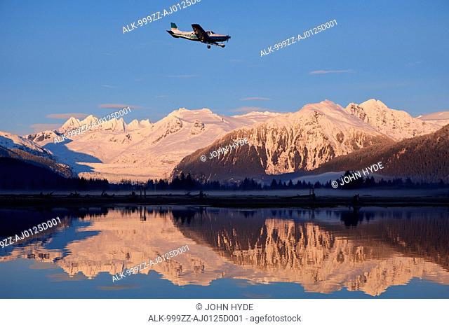 Small plane on approach to the Juneau International Airport passes in front of Mendenhall Glacier and the Coast Range at sunset, Juneau, Southeast Alaska