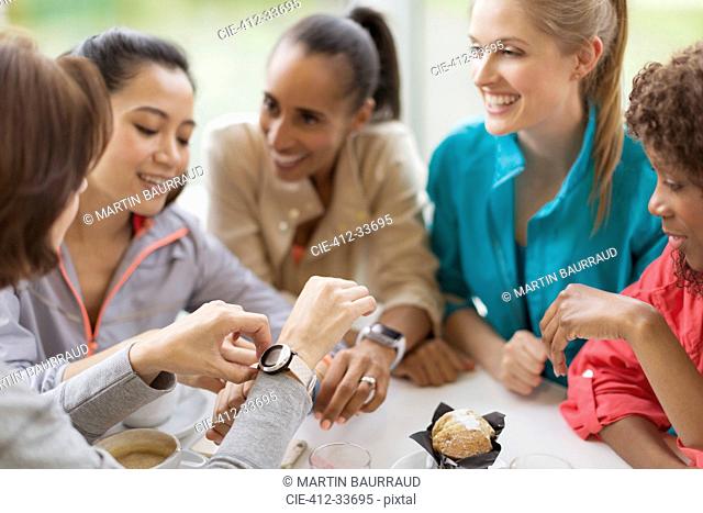 Smiling women friends looking at smart watches in cafe