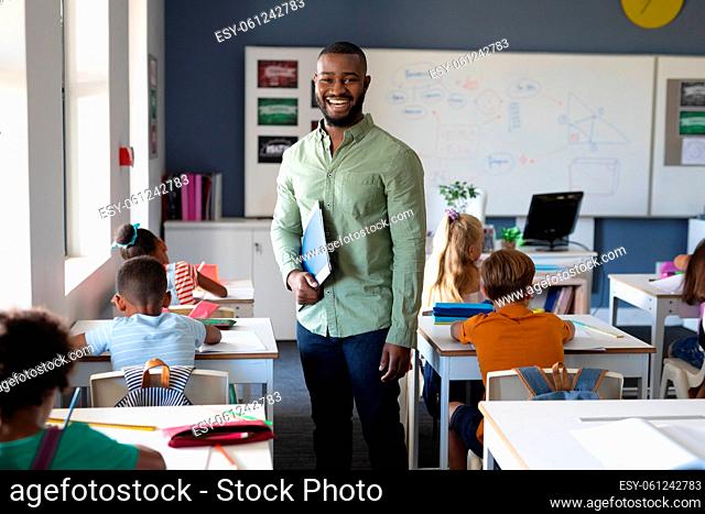 Portrait of smiling african american young male teacher standing by multiracial elementary students