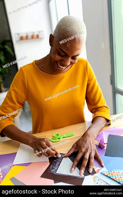 Smiling origami artist sitting in studio folding colorful paper