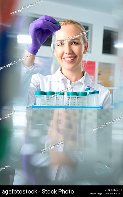portrait of young woman scientist in lab analyzing liquid in retort