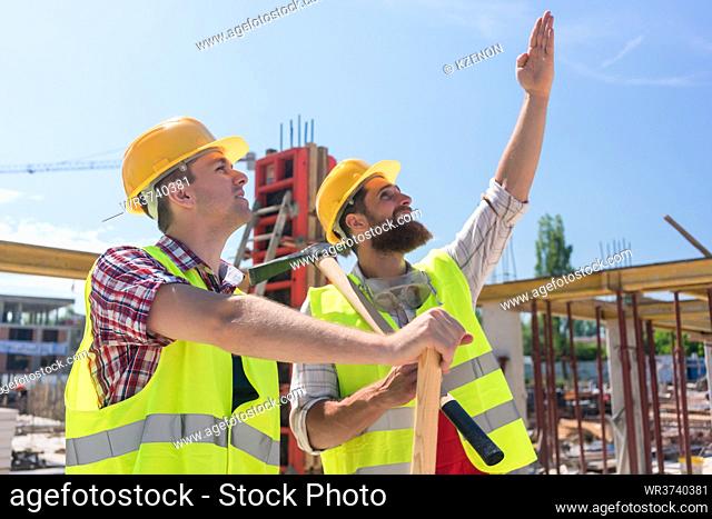 Confident and determined young worker pointing up while imagining with his colleague the height of a building under construction