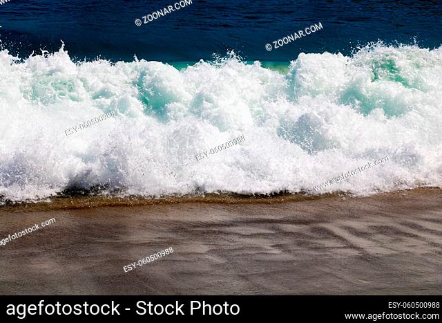 Soft wave of the sea on the sand beach with sunlight. Tropical sandy beach background with copy space. Top down view