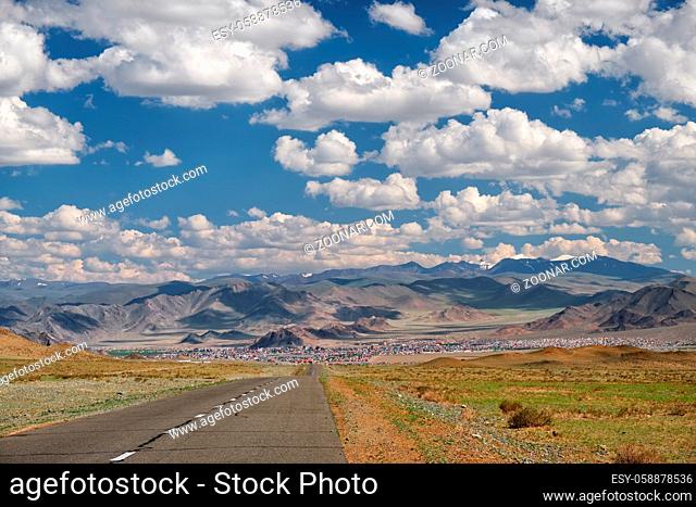 Empty Asphalt road in Mongolia with mongolian town Bayan-Olgii (Bayan-Ulgii or Ulgii) on background under blue sky