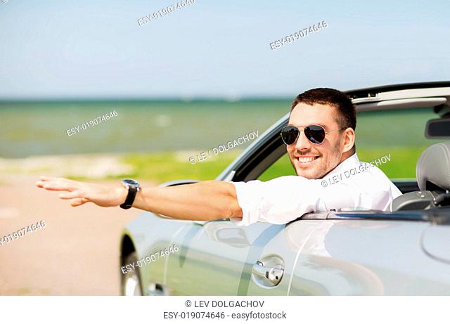 auto business, transport, leisure and people concept - happy man driving cabriolet car and waving hand outdoors