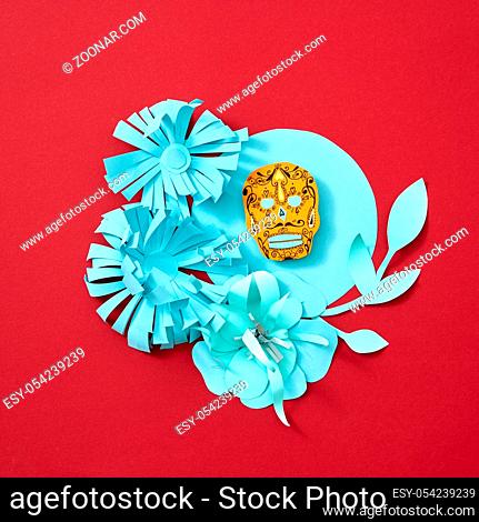 Handcraft paper flowers and leaves decorate the blue frame with Calaveras attribute of the Mexican holiday of Calaca on a red background with space for text