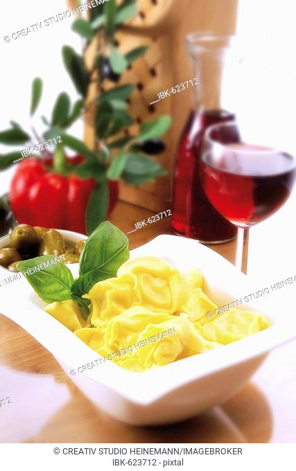 Italian ambiance: tortellini with basil, red wine, olives and an olive twig
