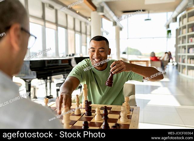 Happy businessman picking up chess piece playing board game with colleague in office