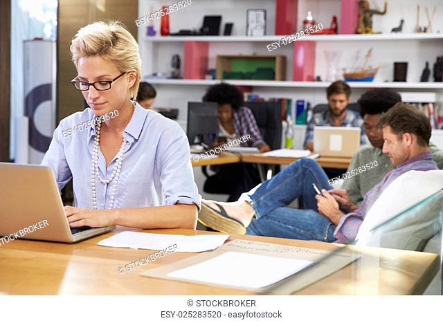 Businesswoman Working On Laptop In Busy Office