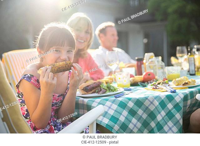 Girl eating corncob at table in backyard