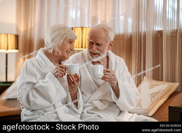 Morning. A senior couple in white robes having coffee and talking