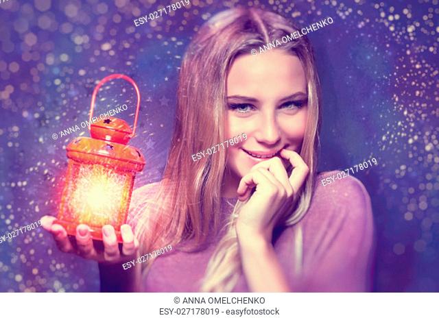 Portrait of a cute blond girl holding on hand red retro style glowing lantern over night starry sky background, magical Christmas fairytale, enjoying Xmas eve