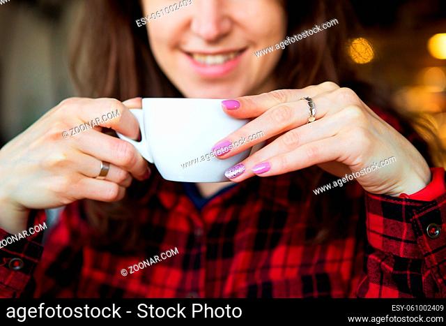 The girl smiles while holding a cup of coffee. Close up