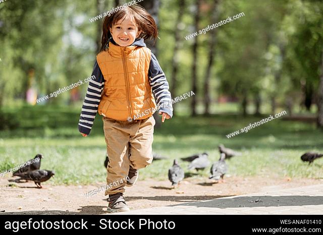 Happy boy running amidst pigeons at park