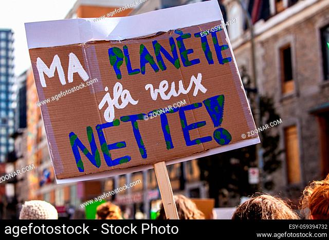 A close-up view of a French sign reading my planet, he wants clean as protestors march for environmental issues on an urban city street