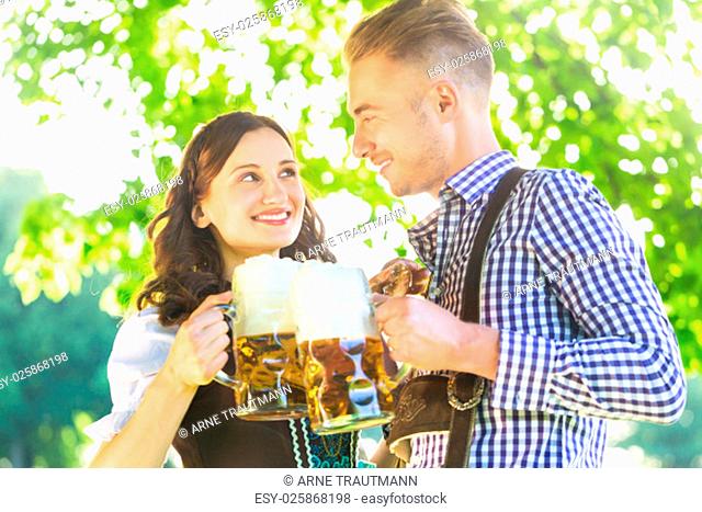 Bayrische Mann und Frau in Tracht trinken Bier draußen aus Maßkrug