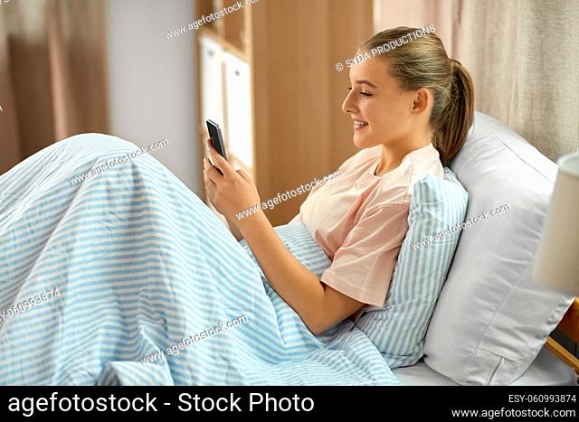 happy girl with smartphone in bed at home