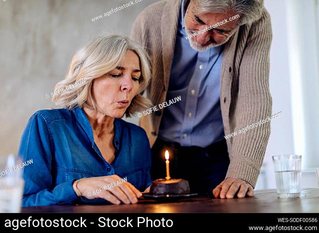 Mature couple celebrating birthday with cake in kitchen at home