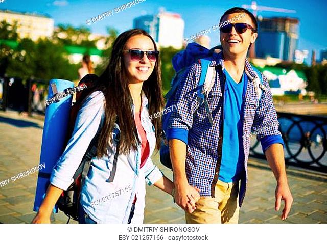 Affectionate couple with rucksacks enjoying weekend walk around the city