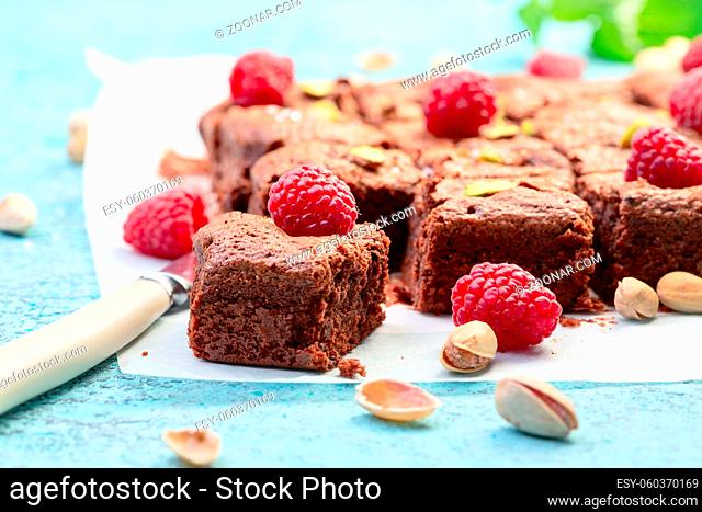 Traditional brownies made of dark chocolate with raspberries, sea salt and pistachios cut into pieces on a sheet of parchment, selective focus