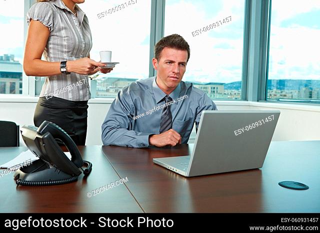 Secretary serving coffee. Businessman working on laptop computer at office