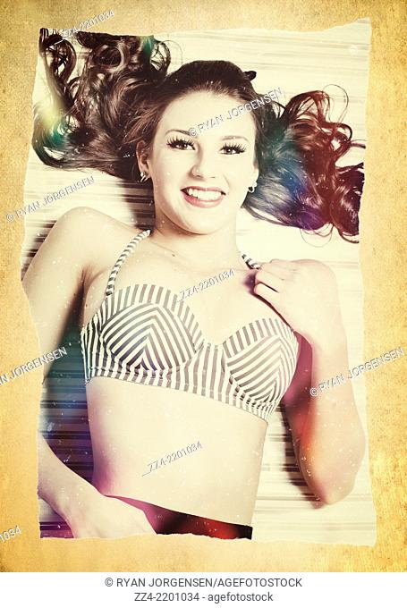 Old ripped and torn photograph with frayed edges of a beautiful young vintage beach girl smiling while relaxing in retro stripe bikini on paper background