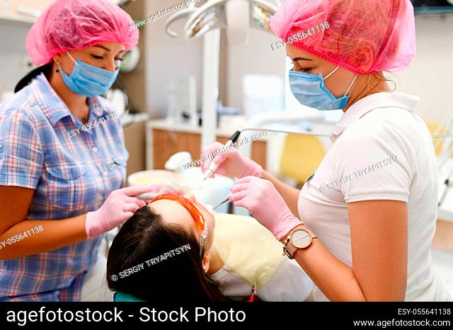Female dentist and assistant are treats patient in clinic, stomatology. Doctor in uniform, medical worker, medicine and health, professional teeth care