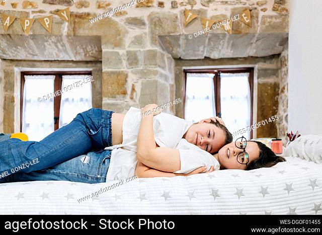 Daughter and mother embracing each other while lying on bed at home