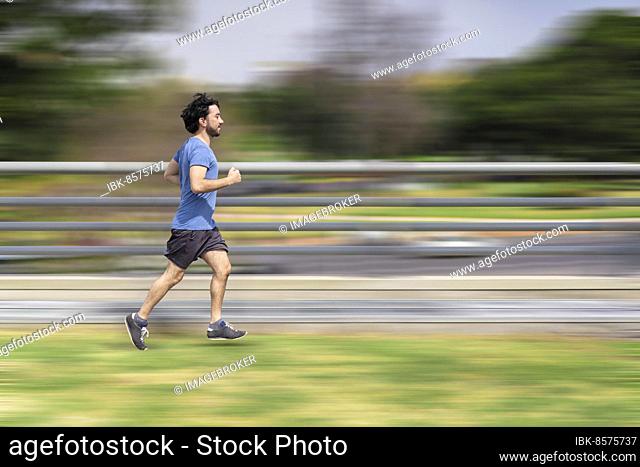 Portrait of handsome attractive mature bearded athletic latin man guy 40s in casual blue t-shirt running at a park. Speed concept