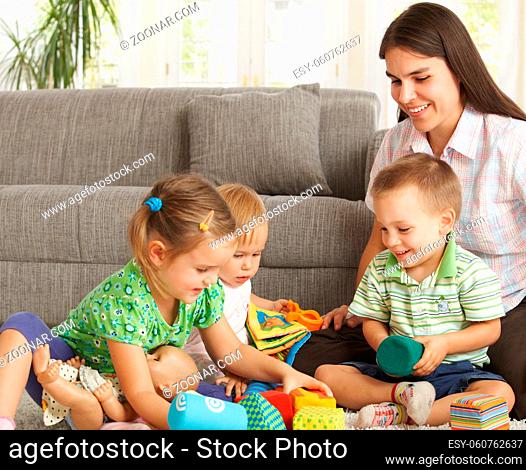 Happy mother and 3 children sitting on floor at home playing together smiling