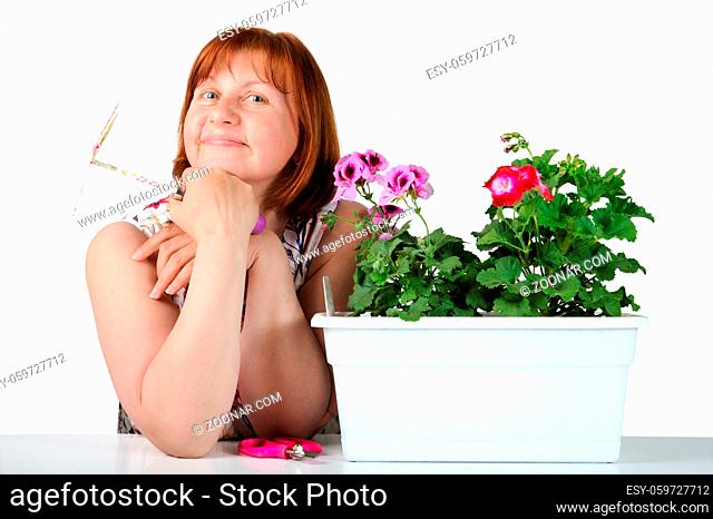 Portrait of pretty middle-aged woman with pelargoniums in a flower pot