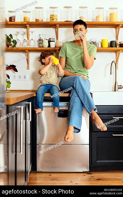 Mother and son having drinks sitting on kitchen counter at home