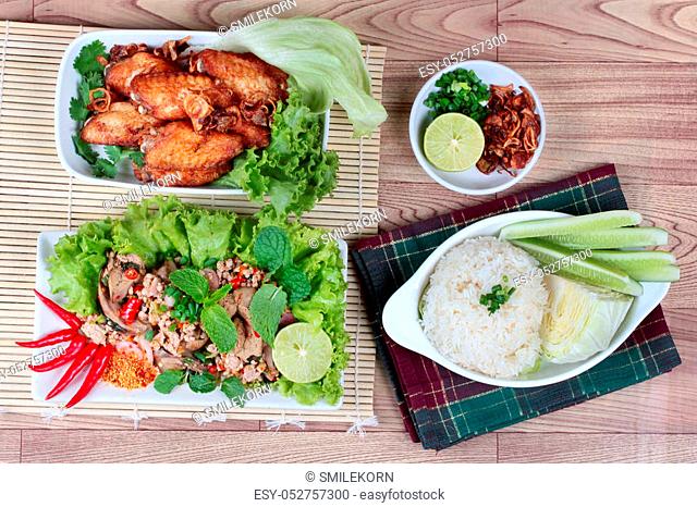 A dish of sticky rice with cucumber and cabbage served side dish as a disk of fried chicken topped fried sliced red onion and spicy sour chicken salad are...