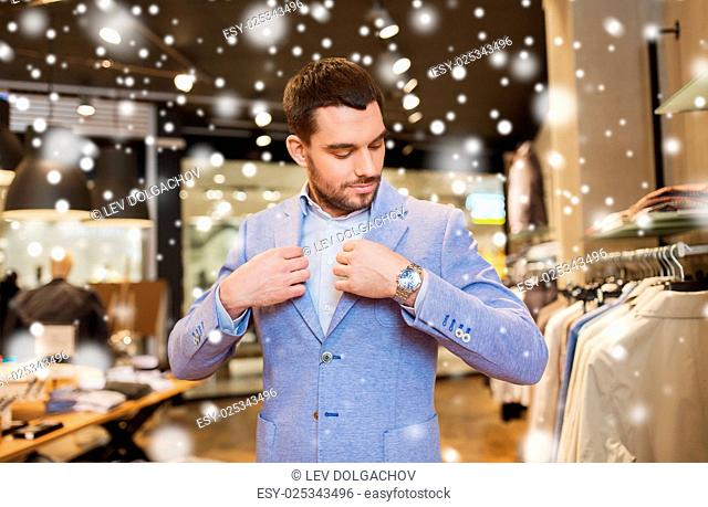 sale, shopping, fashion, style and people concept - elegant young man choosing and trying jacket on in mall or clothing store over snow
