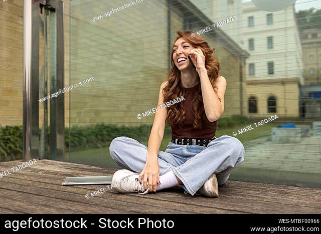 Cheerful woman talking on mobile phone while sitting in front of wall