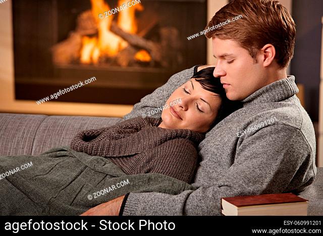 Young couple hugging on sofa in front of fireplace at home, woman sleeping