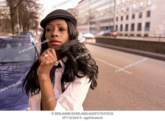 stylish emotional woman in evening sunlight at street, individual look, African Angolan descent, in city Munich, Germany