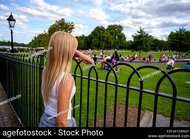 Female tourist watching people playing in the water in the Diana Memorial Fountain, Hyde Park, London, United Kingdom