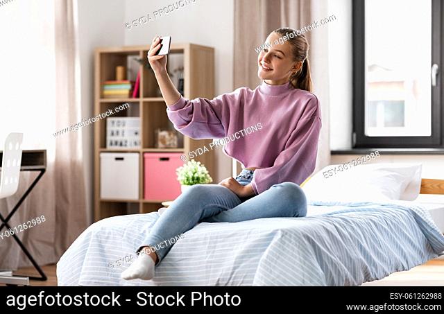 happy girl with smartphone taking selfie at home