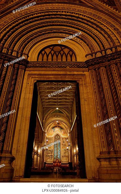 Exterior view of front entrance of Orvieto Duomo illuminated at night, seen from low angle, showing arched doorway, and illuminated interior, central nave