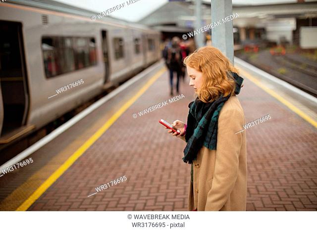 Young woman standing on railway platform using her mobile phone