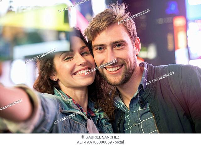 Young couple taking selfie in illuminated city street