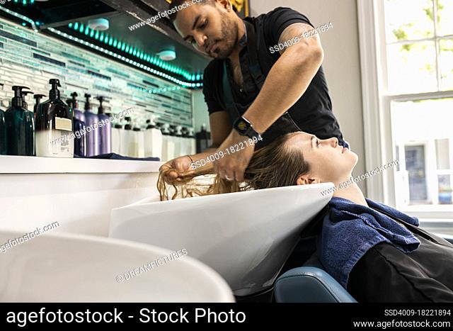 Stylist washing young woman?s hair in sink at boutique salon